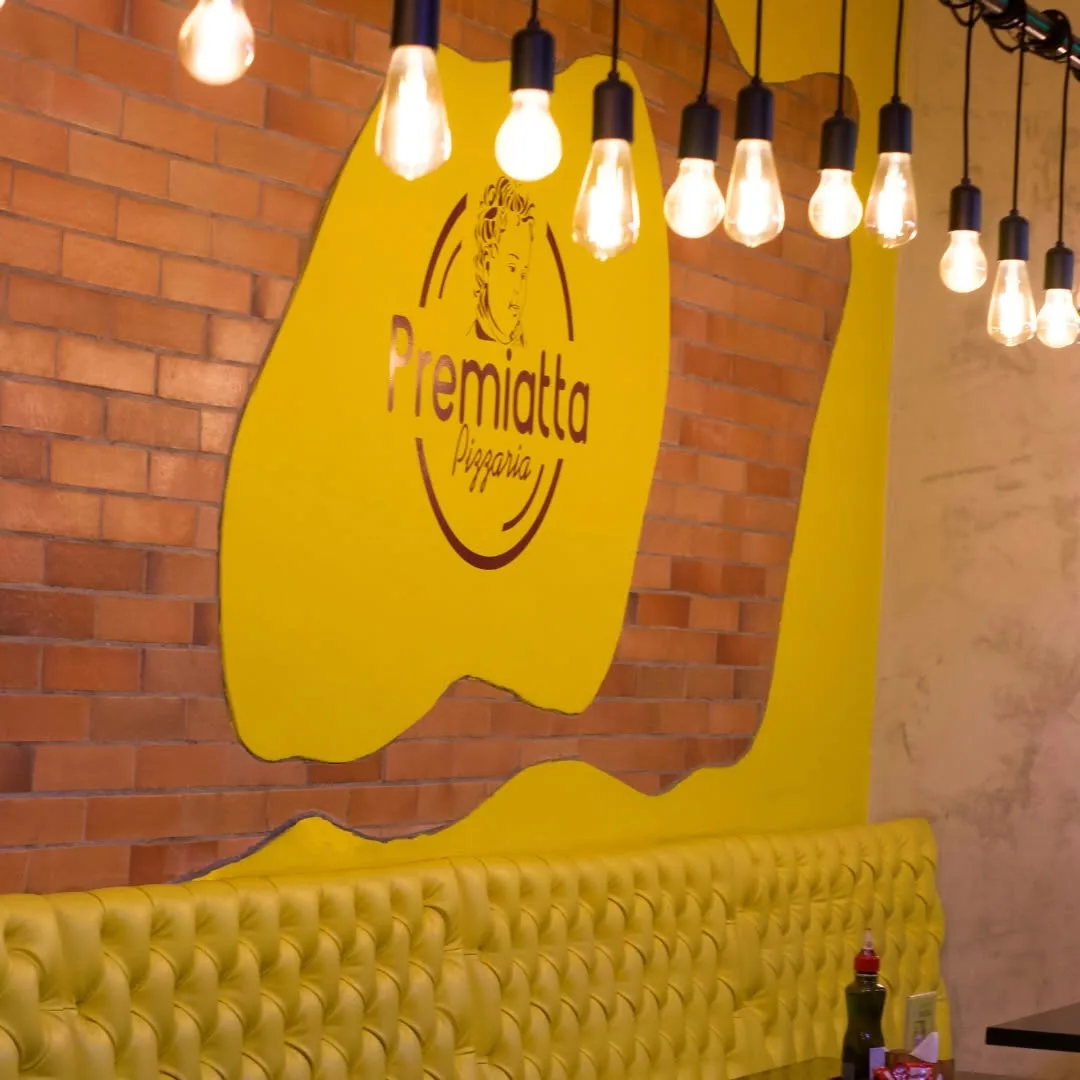 Salão com parede amarela, logo da Premiatta e luminárias